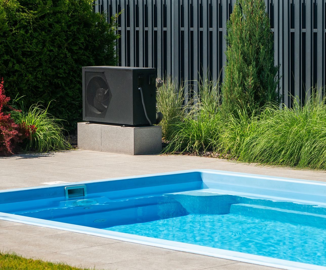 There is a swimming pool in the backyard with a fence in the background.