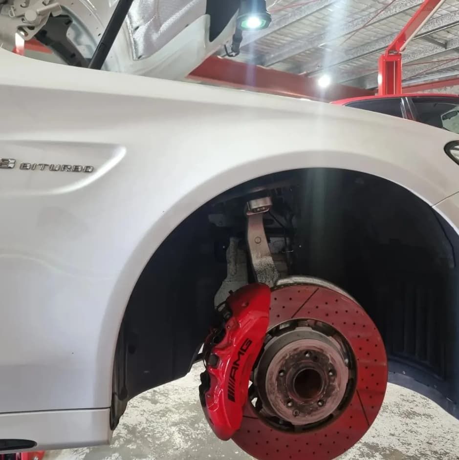 White car with red brake calipers and rotors; wheel removed, car in shop — MC Automotive Service & Repairs in Maitland, NSW