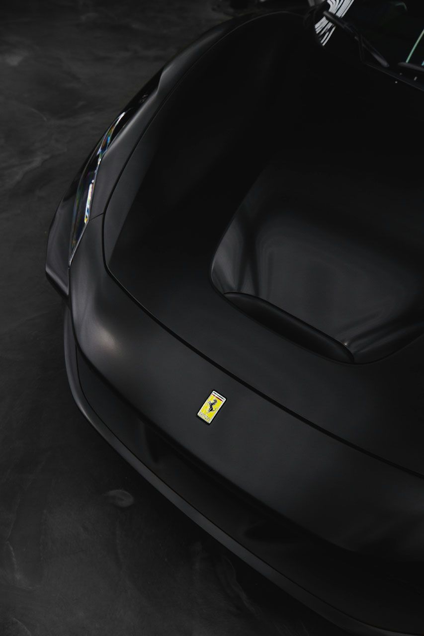 Black Ferrari sports car, low-angle view of the hood with yellow emblem, in a dark setting.