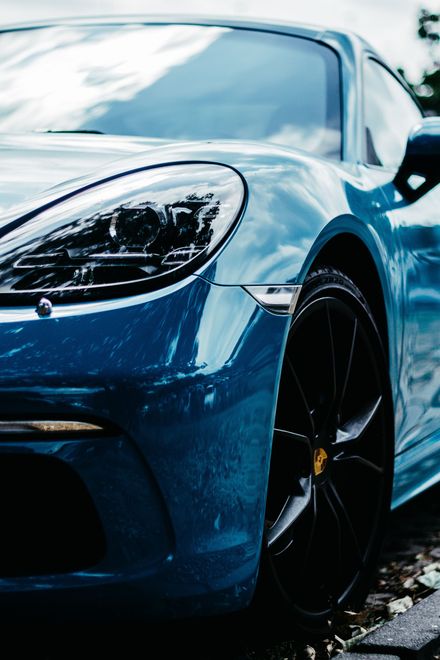 Blue Porsche sports car, black wheels, reflective body, daytime.