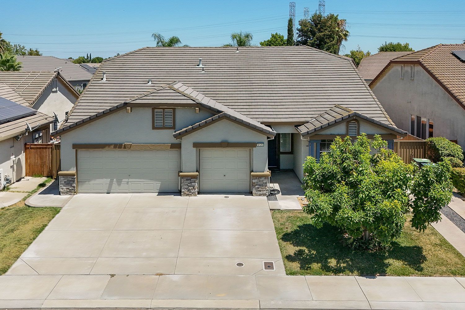 Tan suburban house with a two-car garage, concrete driveway, and a small front yard under a blue sky.