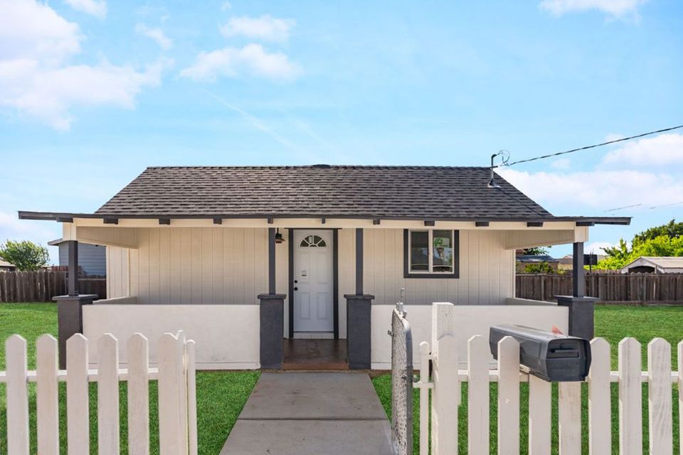 White house with black accents, front porch, picket fence, blue sky, and mailbox.