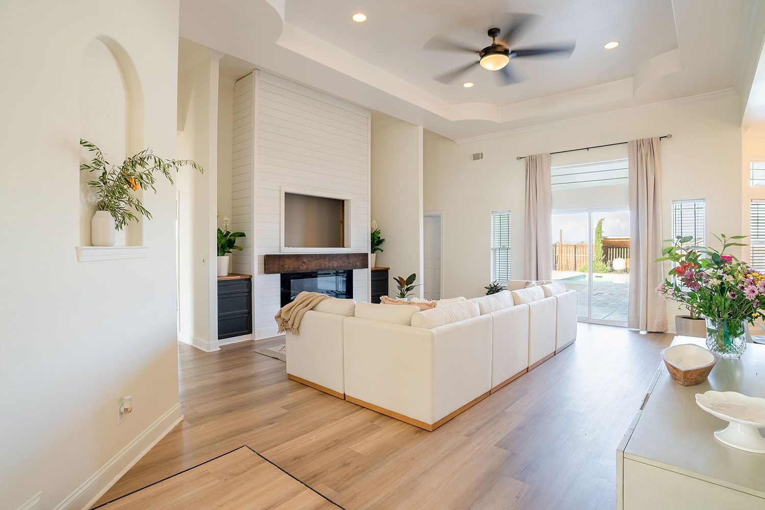 Bright, open-concept living room with white sectional, fireplace, and large windows overlooking a patio.