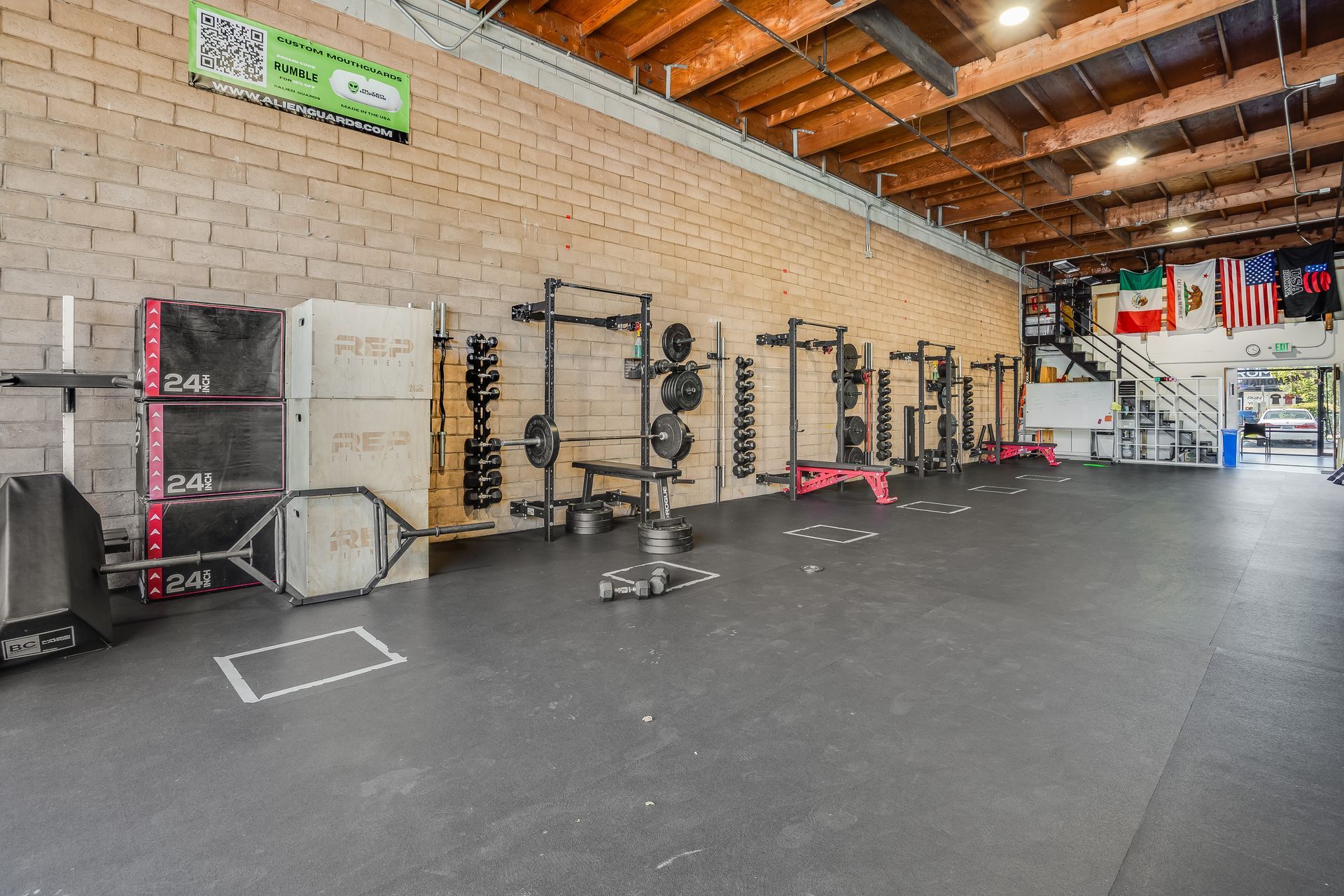 Weightlifting gym with equipment against a brick wall. Gray floor, wooden ceiling.