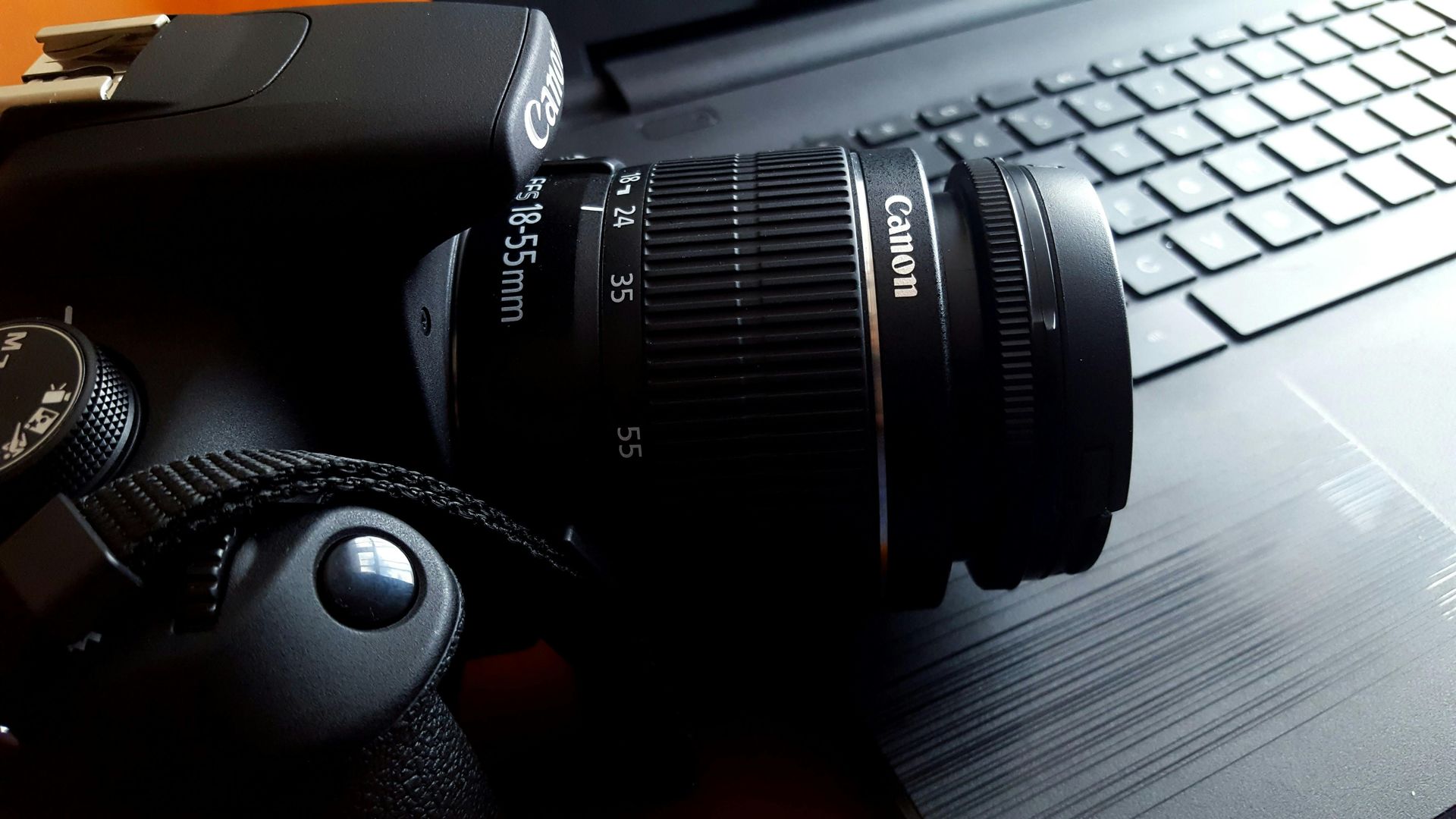 A Canon DSLR camera with lens sitting on a laptop keyboard, partially illuminated.