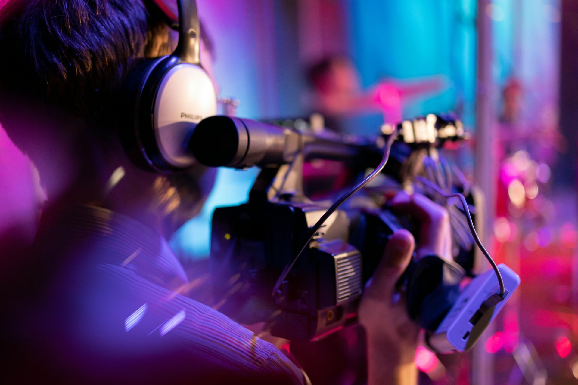 Cameraman with headphones filming in a brightly lit, purple and blue setting.