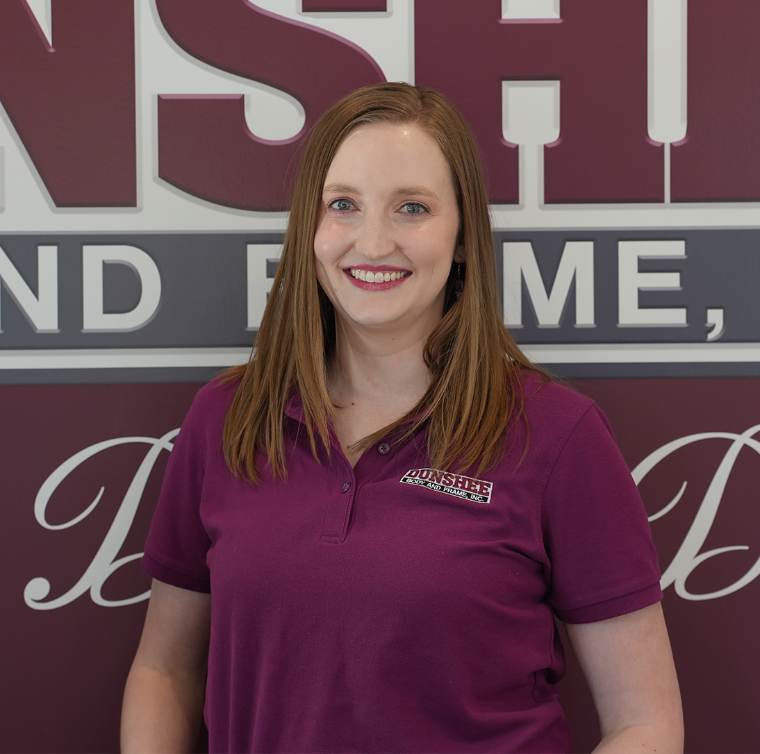 Woman in a maroon polo smiling in front of a company sign and wall logo.