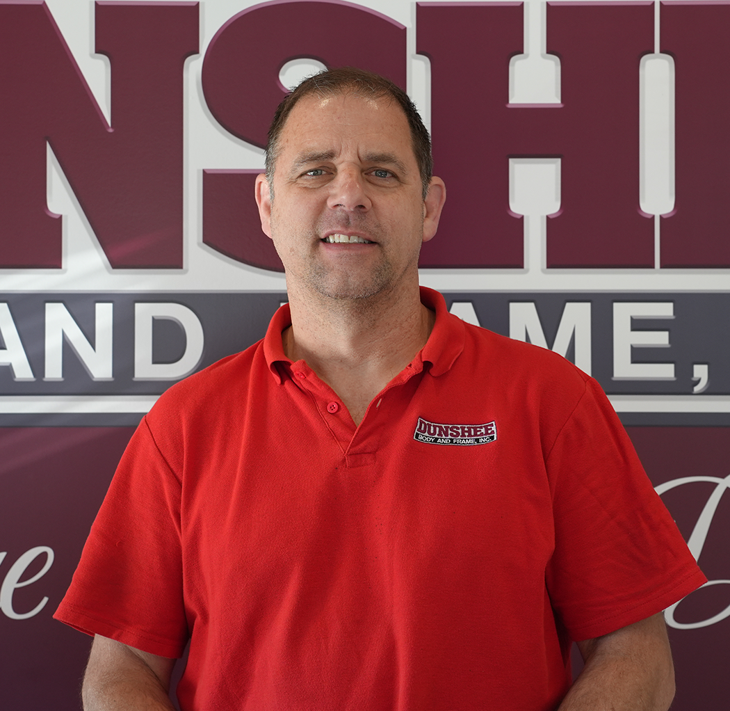Man in a red polo shirt standing in front of a maroon and white sign