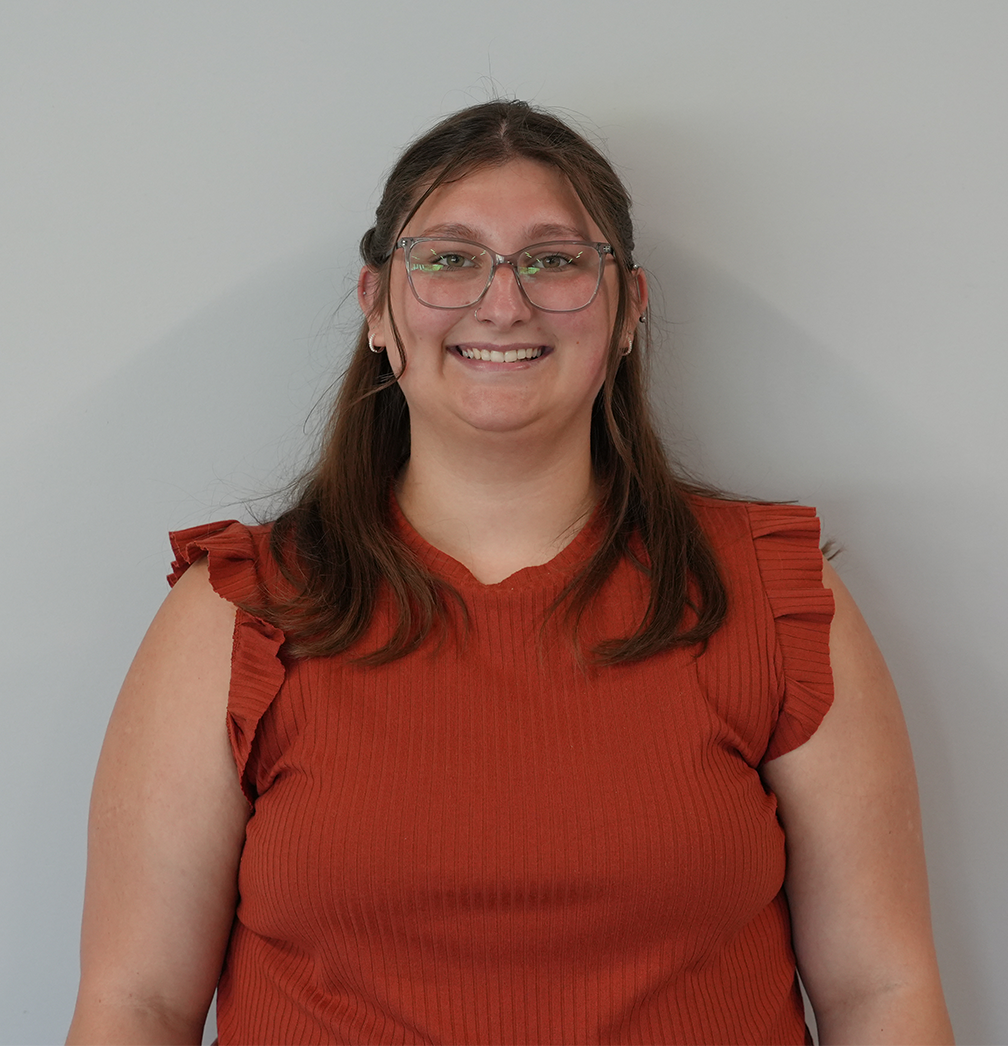 Smiling person with glasses wearing a red ruffled top against a plain gray background
