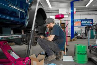 Mechanic using a tool to repair a silver car door in a garage