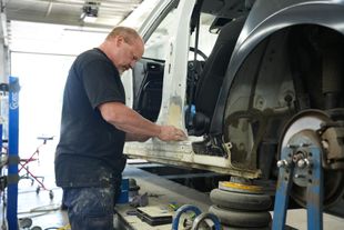 Mechanic inspecting the front of a silver car in an auto repair shop with the hood open