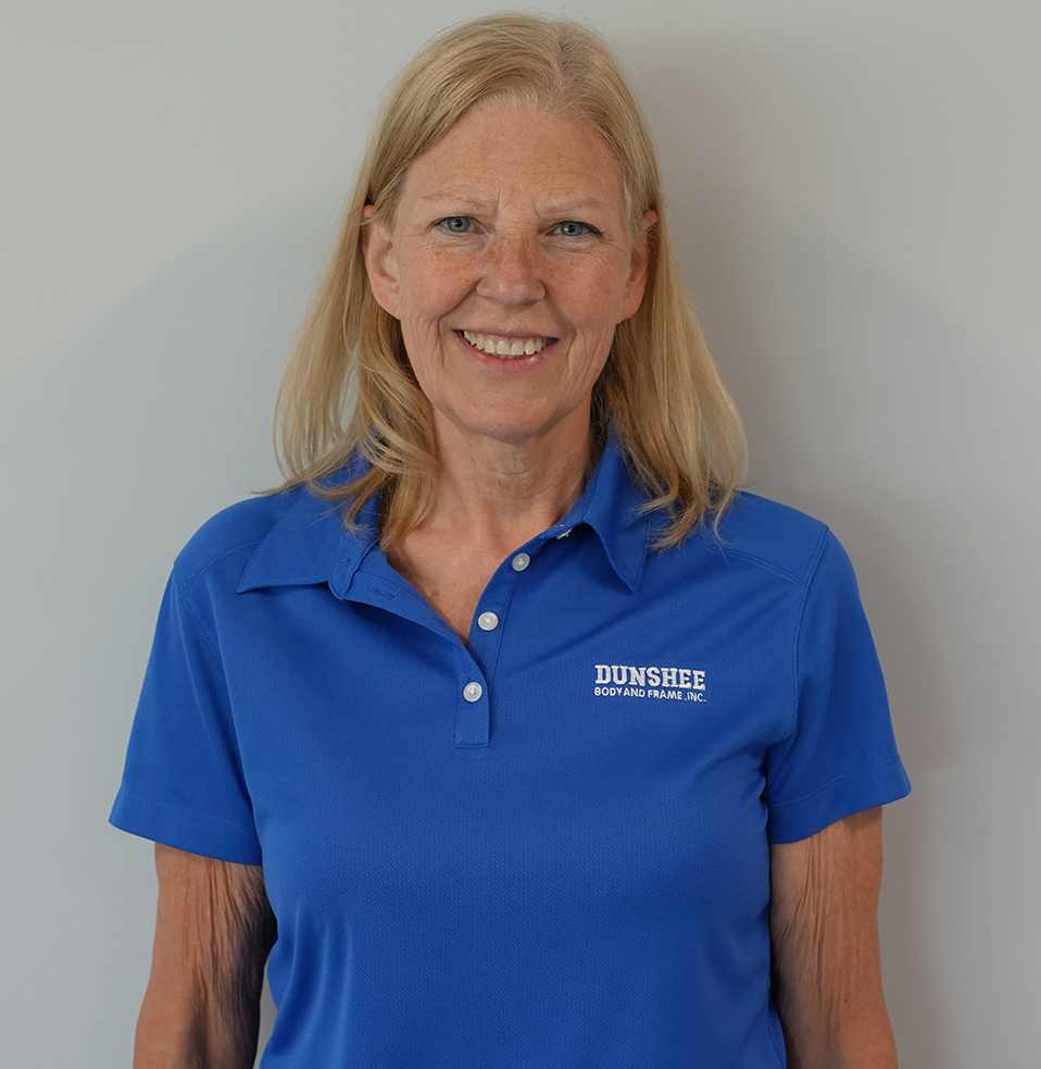 Woman in blue polo shirt standing against a plain gray background, smiling.