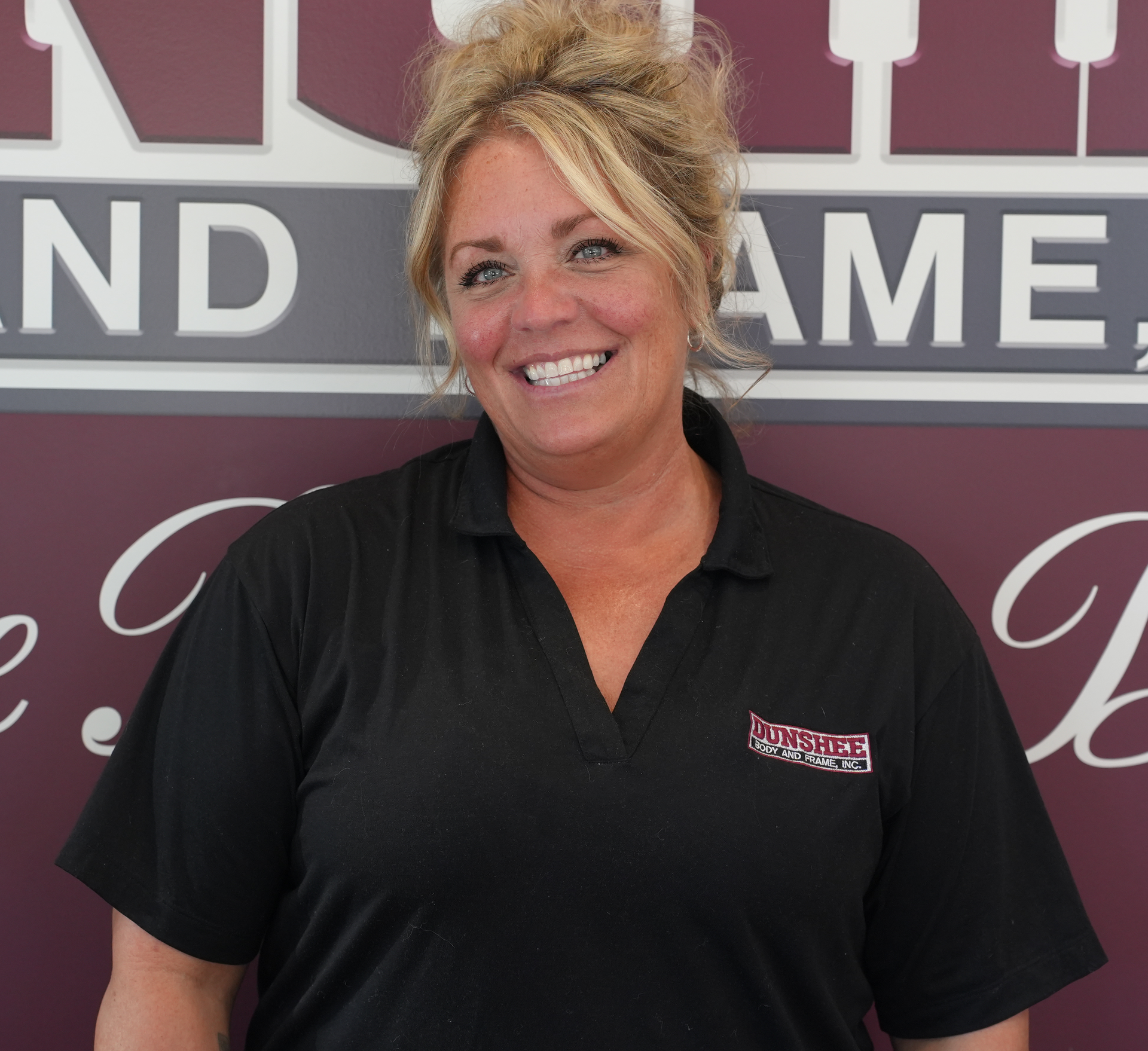 Smiling woman in black polo standing in front of a maroon and gray signboard