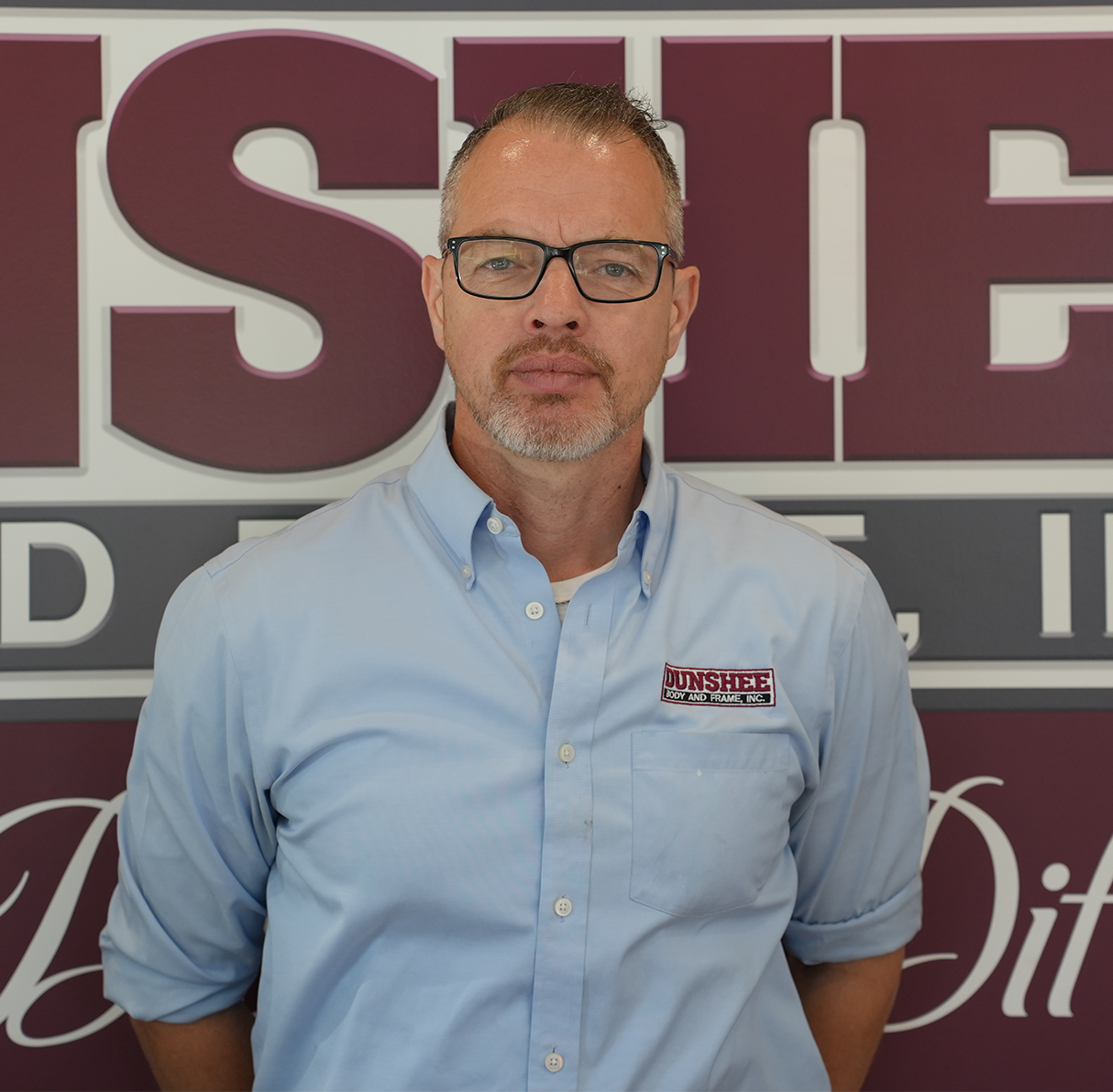 Man in glasses and light blue shirt standing in front of a maroon and white sign