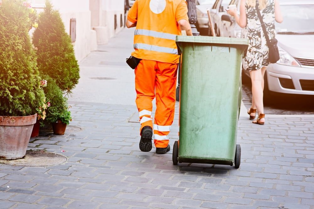 A Man in Orange Pants Is Pushing a Green Trash Can Down a Sidewalk — Acres 2 Mow in Port Stephens, NSW