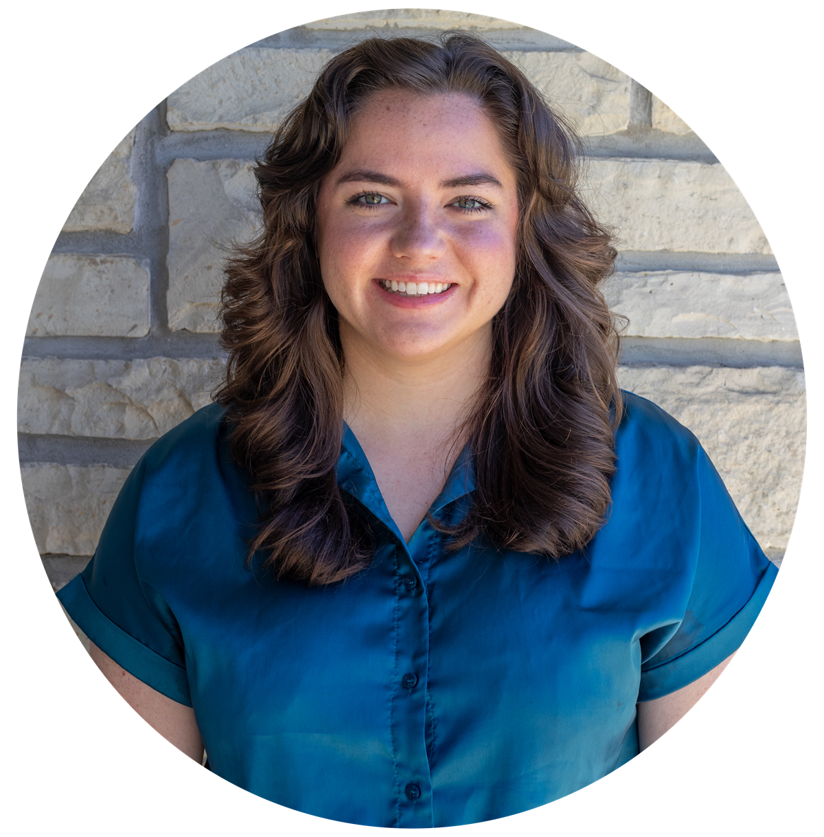 A woman in a blue shirt is smiling in front of a brick wall
