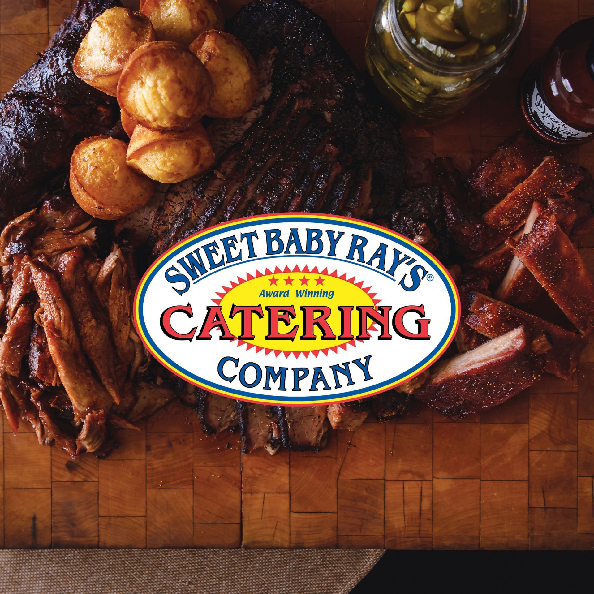 logo in front of barbecue meats, pickles, and cornbread muffins on a wood board