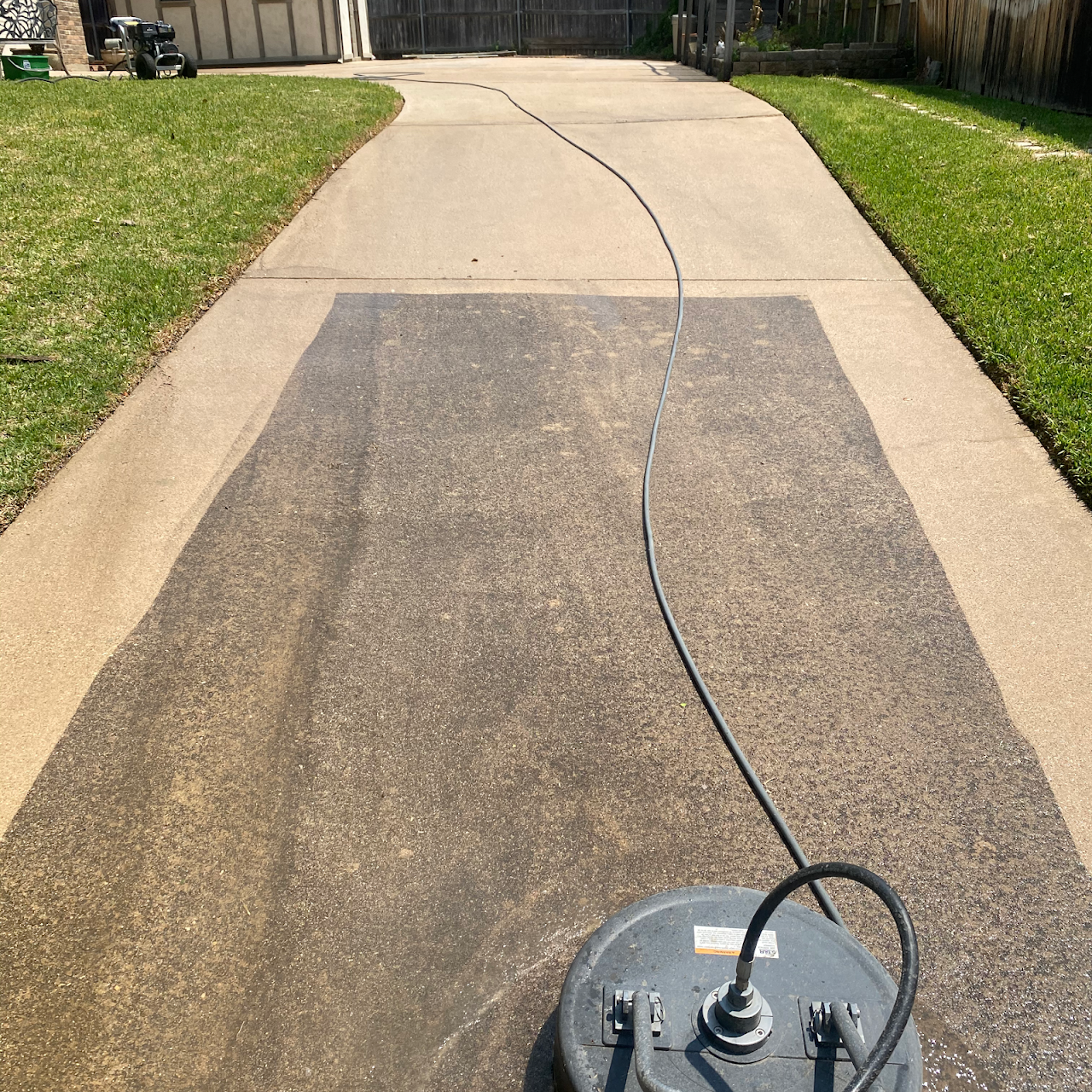 Pressure washing a concrete driveway, showing the cleaned section.