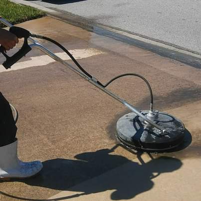 Person power washing a concrete surface with a circular surface cleaner, removing dirt.