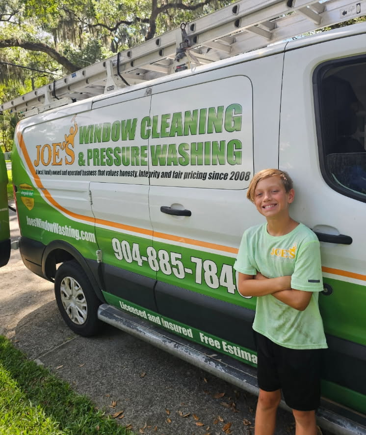 Young boy standing proudly in front of a white and green van advertising