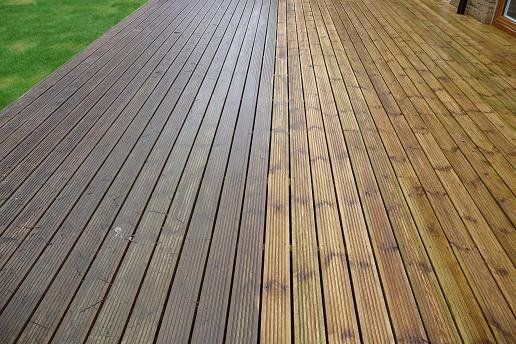 A wooden deck, half weathered and dark, the other half cleaned, showing bright, fresh wood.