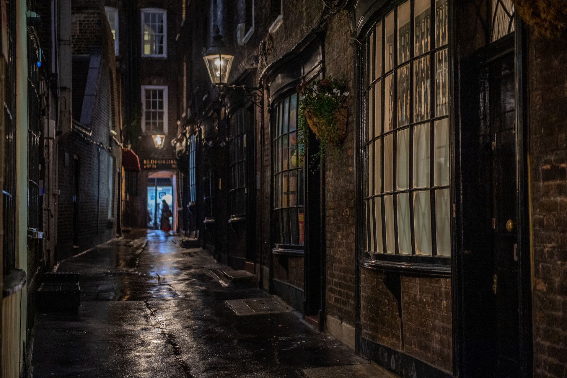 Narrow historic London alley at night with wet cobblestones and shop windows