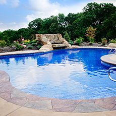 A large swimming pool surrounded by trees and rocks in a backyard.