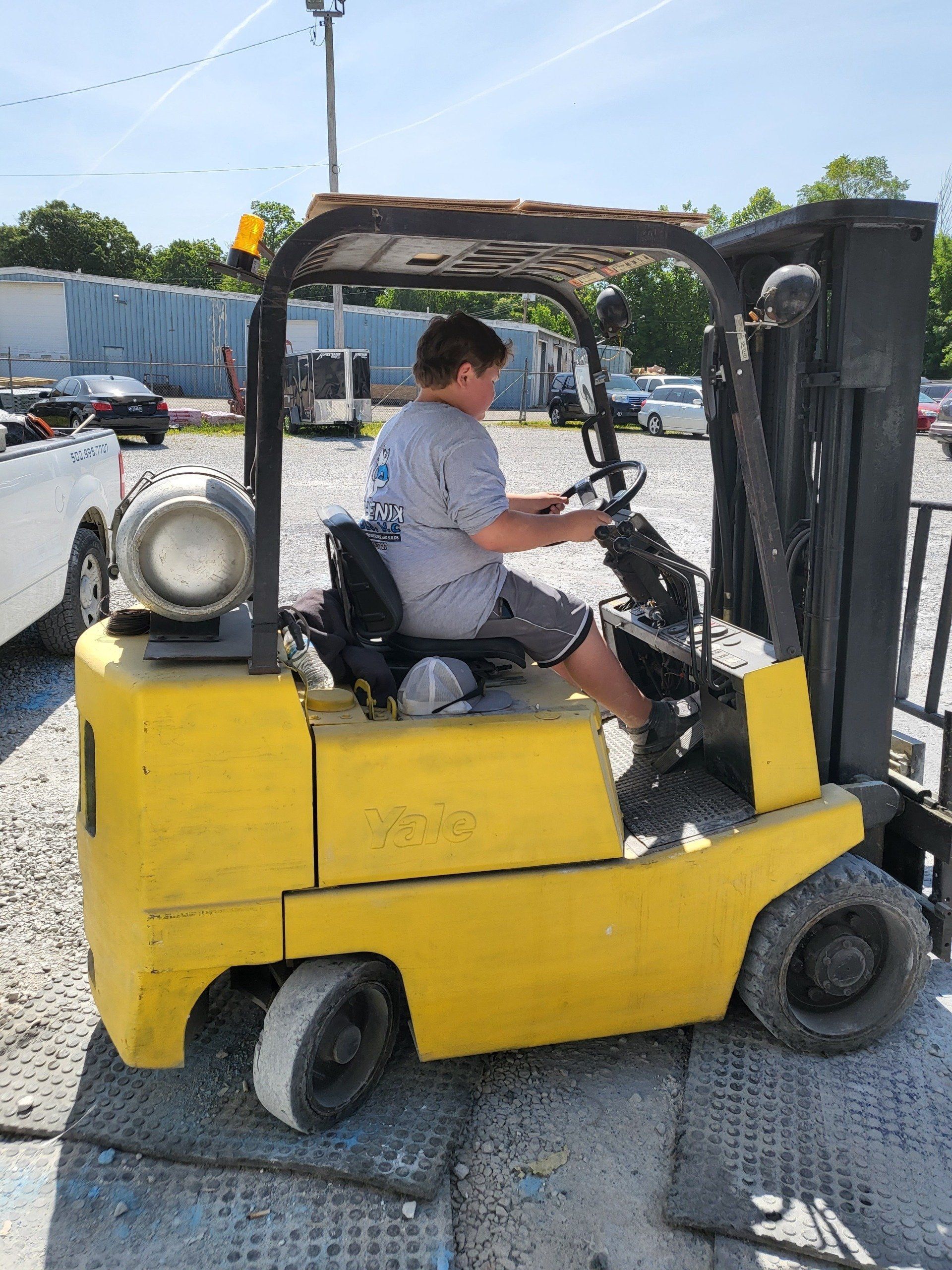 A man is driving a yellow forklift in a parking lot