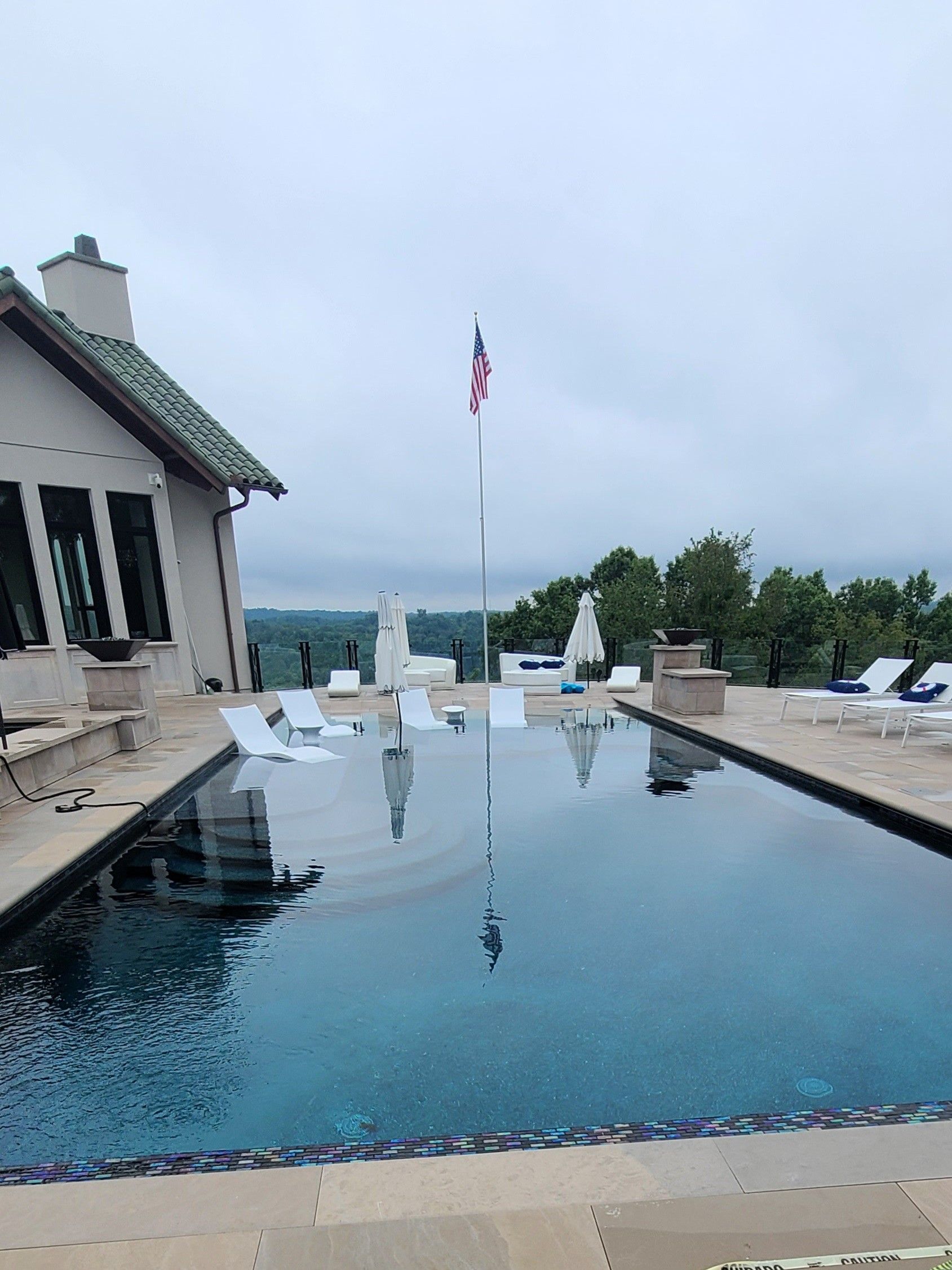 A large swimming pool is surrounded by chairs and a house.