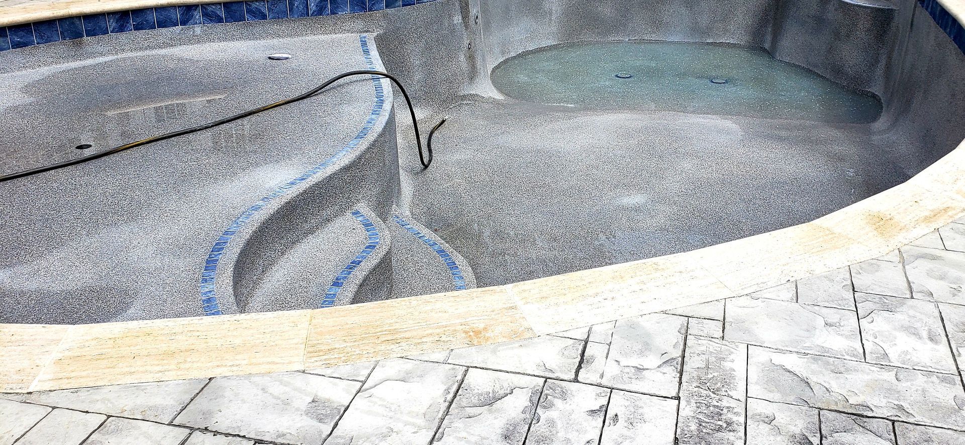 A swimming pool with stairs leading to it and a concrete patio in front of it.