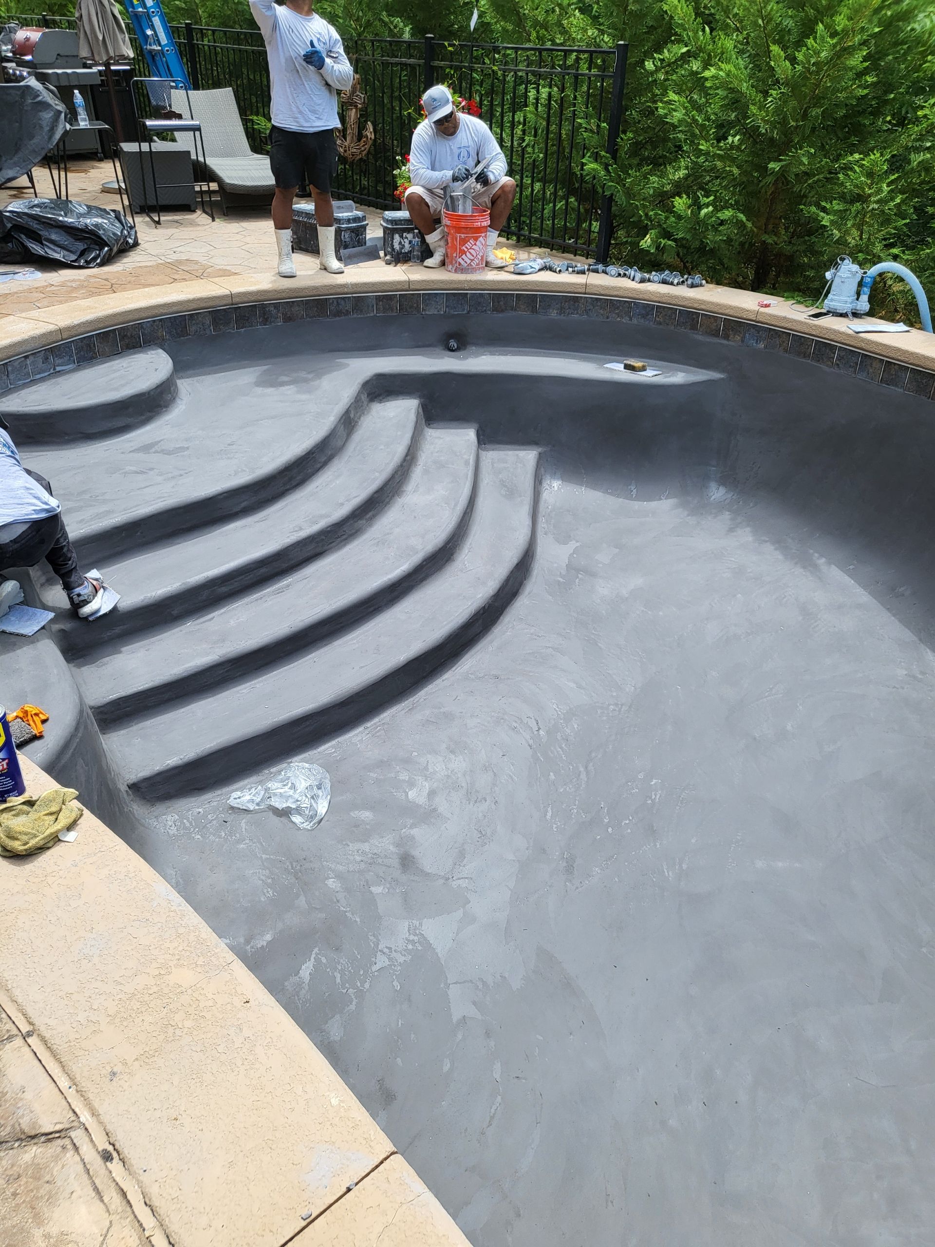 Two men are painting a swimming pool with black paint.