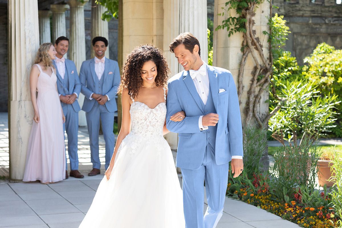 A flower girl and a boy in a suit are running in the grass.