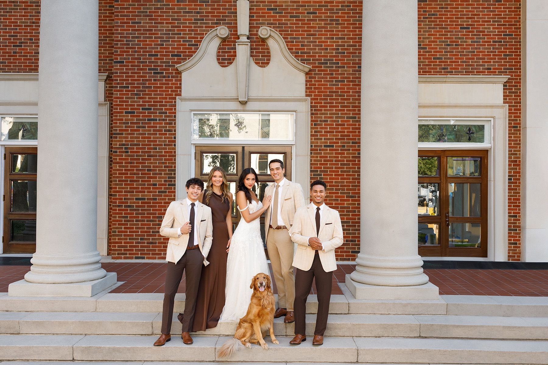 A bride and groom are posing for a picture with their wedding party in a park.