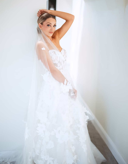 A woman in a wedding dress with a high slit is standing in front of palm trees.