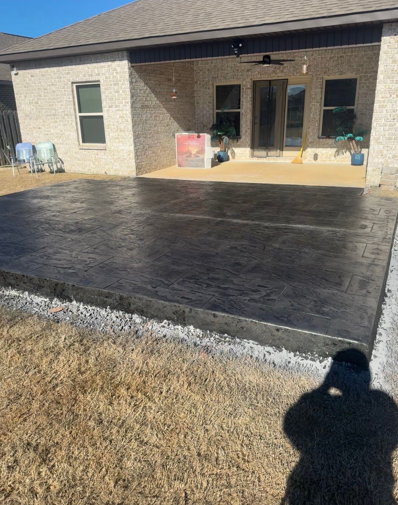 Backyard patio with a freshly poured black concrete slab beside a brick house