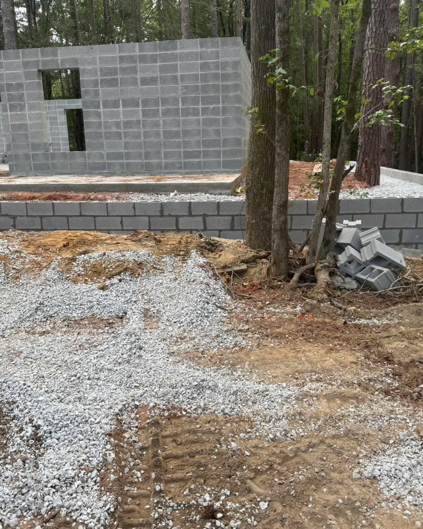 Partially built cinder block wall at a wooded construction site with gravel and trees
