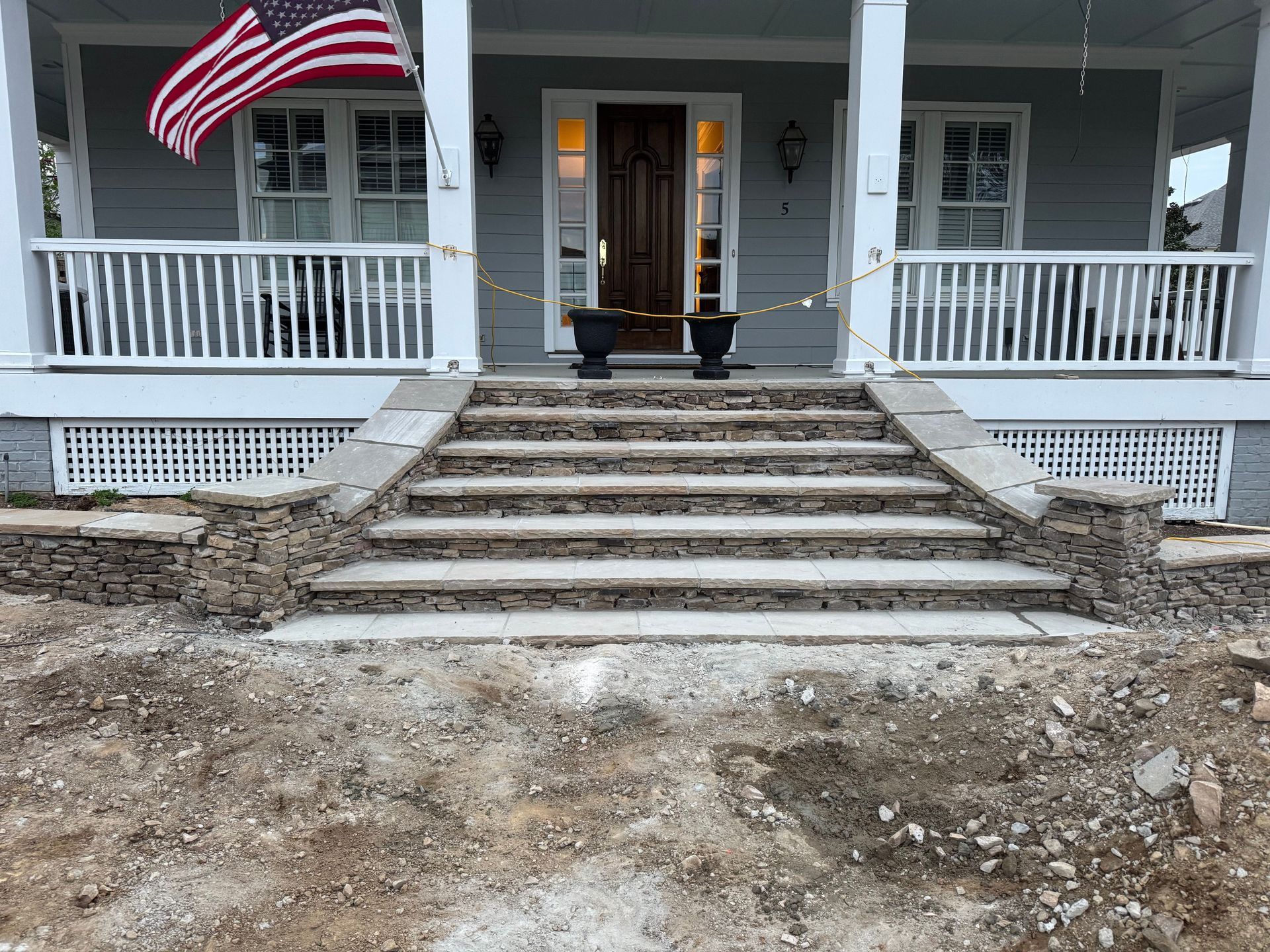 Front porch of a house with an American flag, white railings, and wide stone steps under construction