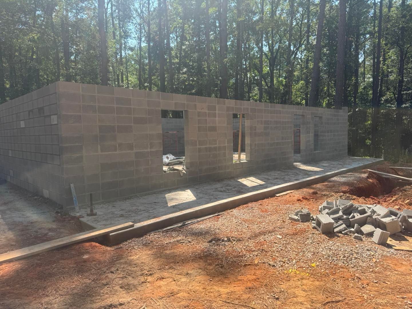 Partially built cinder block structure on a dirt lot, with trees in the background and construction debris nearby