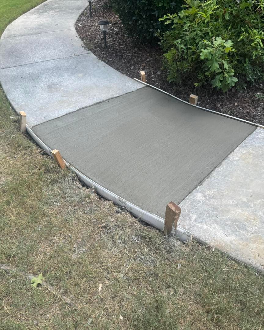 Gray concrete walkway ramp between sidewalks, with wooden stakes and grass along the edge.