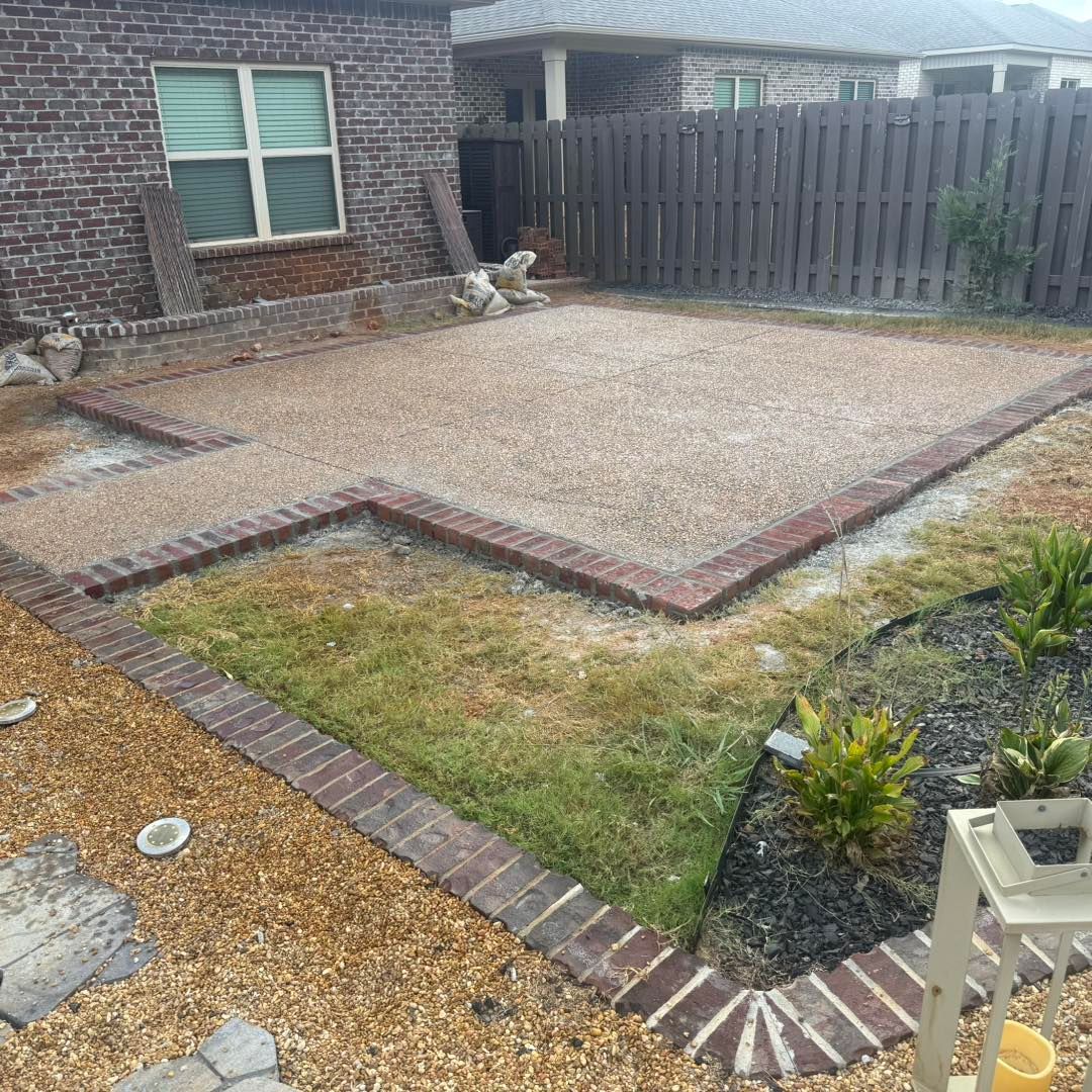 Gravel patio beside a brick house, bordered by red pavers and a small lawn and garden bed.