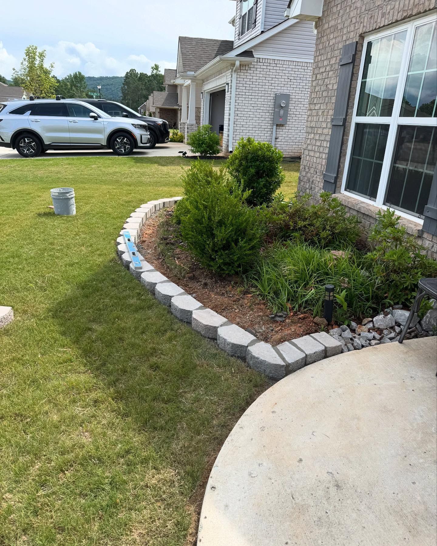 Suburban front yard with a curved stone flower bed, shrubs, lawn, and a silver SUV by the house