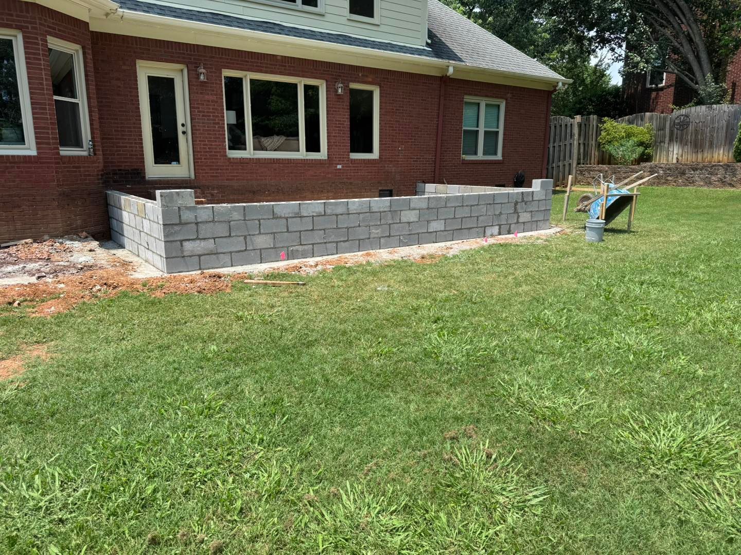 Backyard with a brick house and a low gray block retaining wall along the lawn