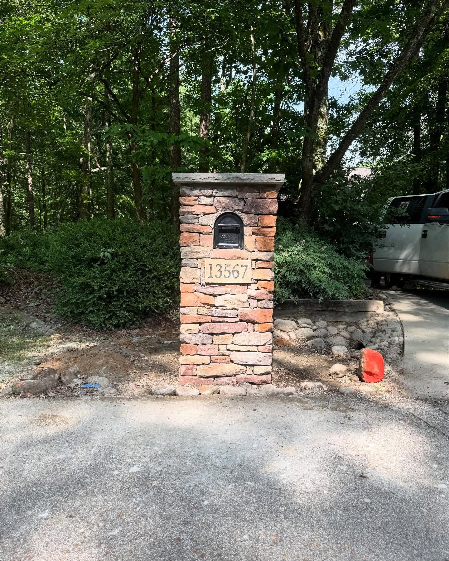 Brick mailbox pillar by a driveway, with a black mailbox, house number 3567, and trees behind it.