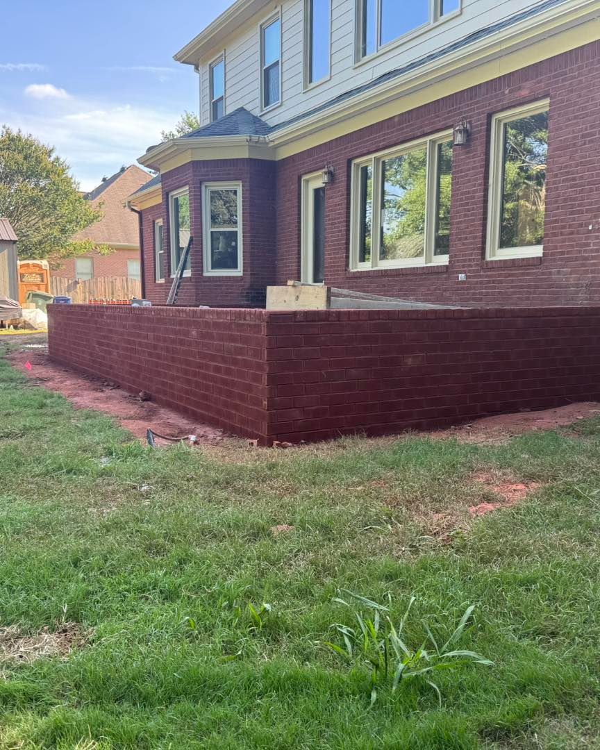 Brick house with maroon deck railing and bay window beside a grassy yard