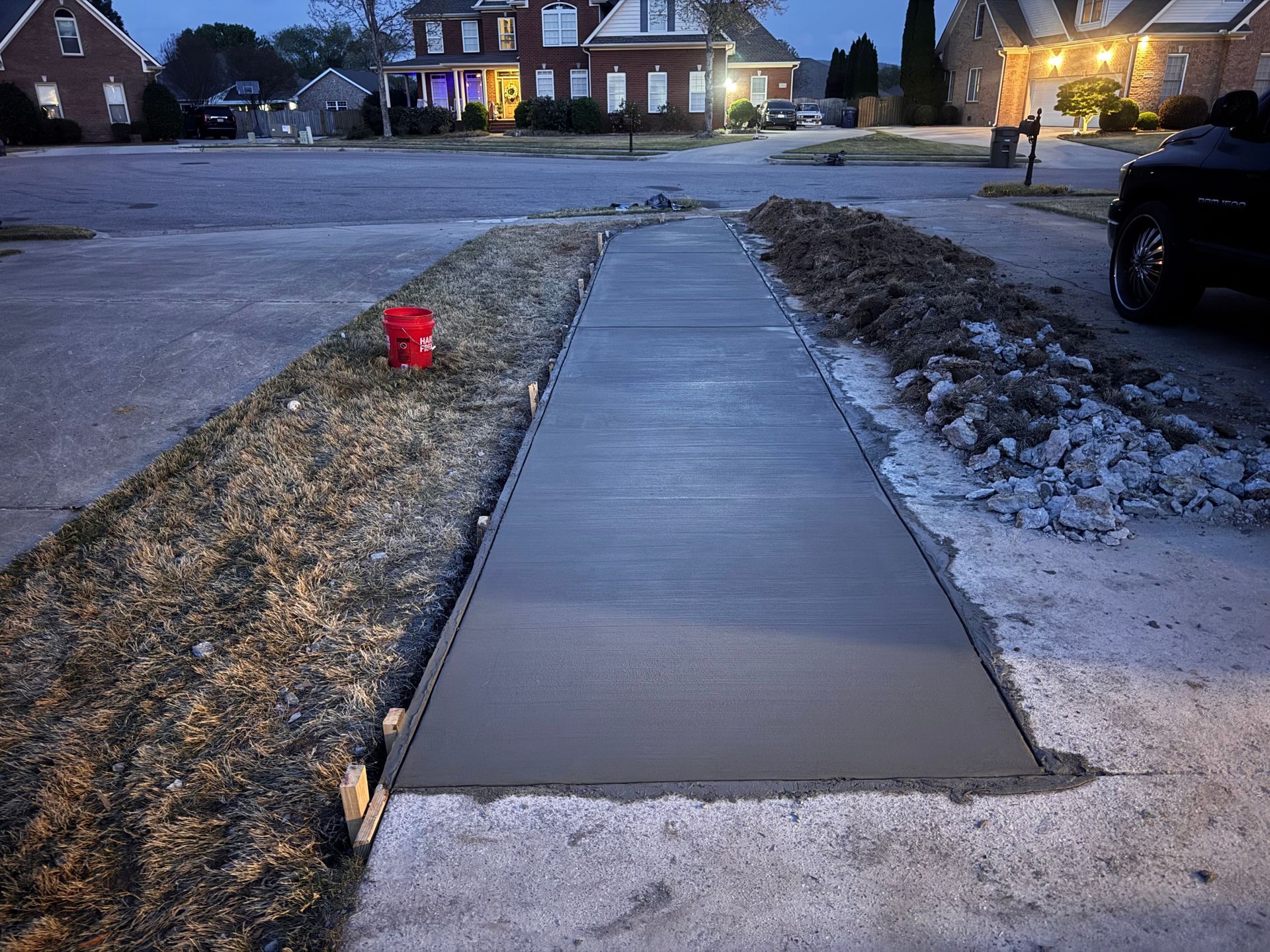 Fresh concrete sidewalk beside snowy grass and a residential street at dusk, with a red fire hydrant nearby