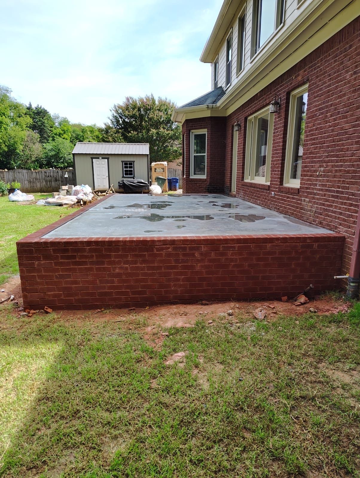 Brick patio beside a house with a red brick retaining wall and a small shed in the yard.