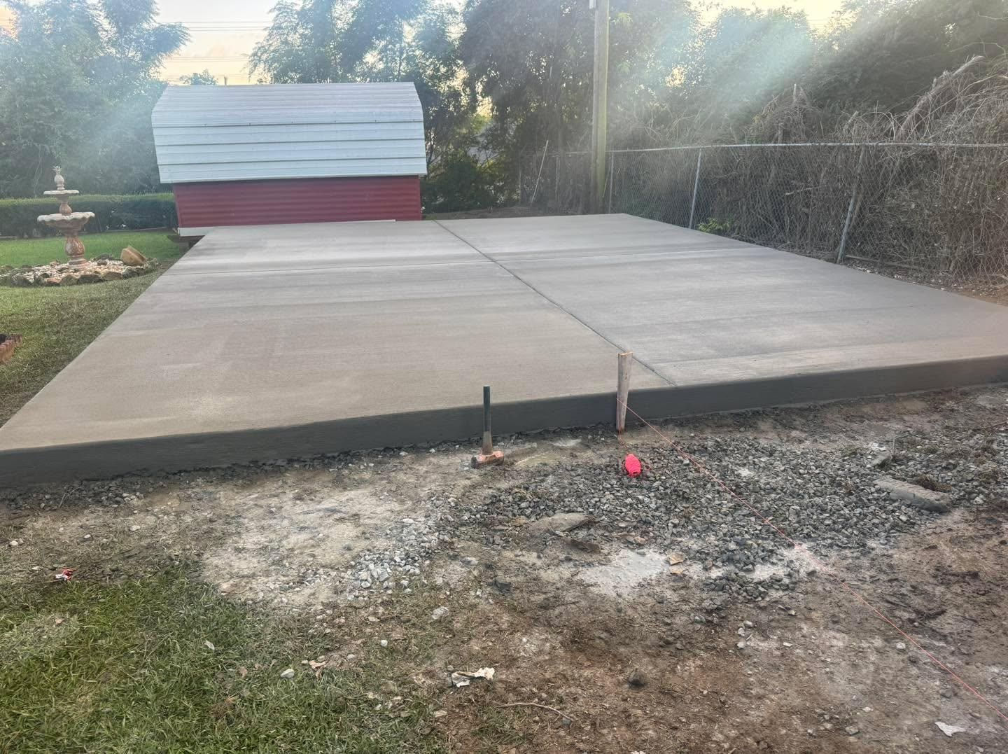 Concrete slab foundation in a yard, with a small red-and-white shed in the background.
