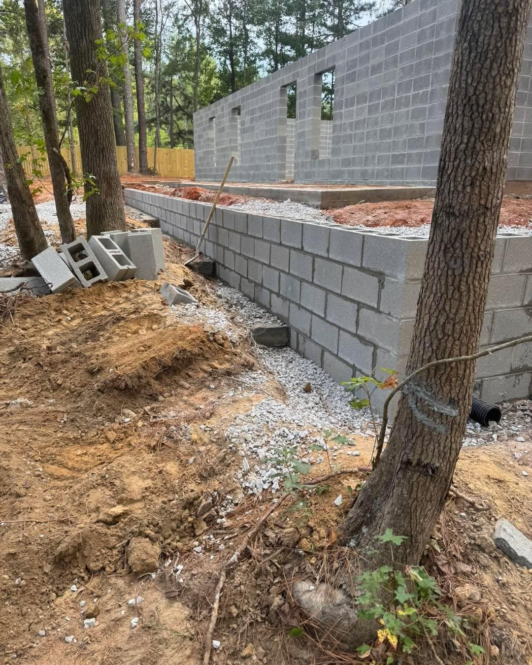 Partially built cinder block wall beside trees in a wooded construction area