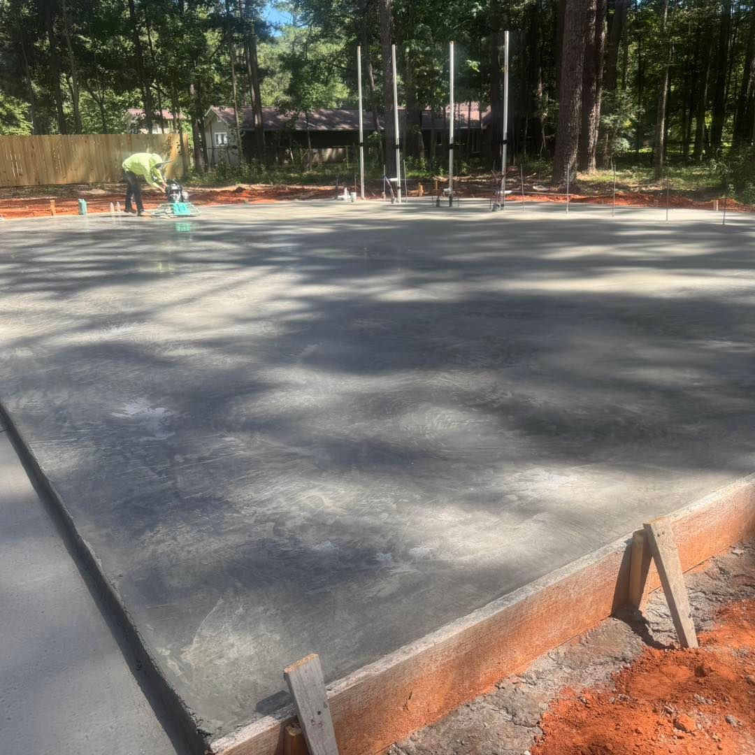 Freshly poured concrete pad with orange formwork in a wooded outdoor area