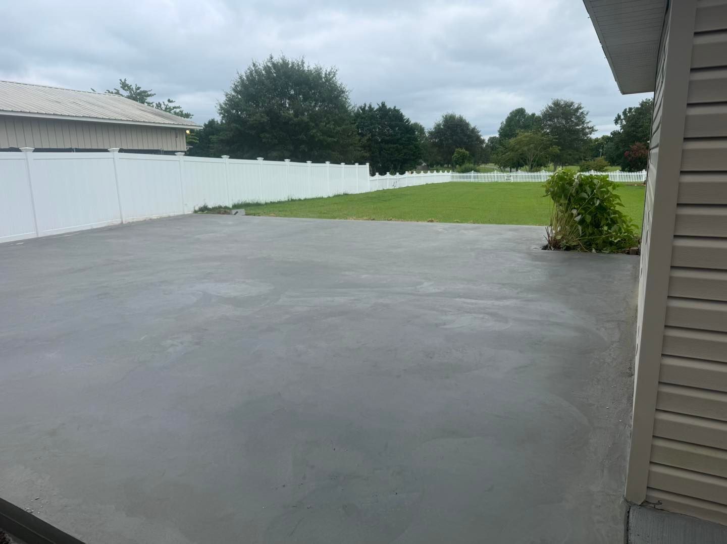 Empty concrete driveway beside a white fence and green lawn under a cloudy sky